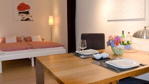 Ein Hotelzimmer mit einem Bett, einem Esstisch gedeckt mit Tellern, Gläsern und Besteck sowie einer Vase mit Blumen.