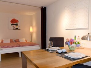 Ein Hotelzimmer mit einem Bett, einem Esstisch gedeckt mit Tellern, Gläsern und Besteck sowie einer Vase mit Blumen.