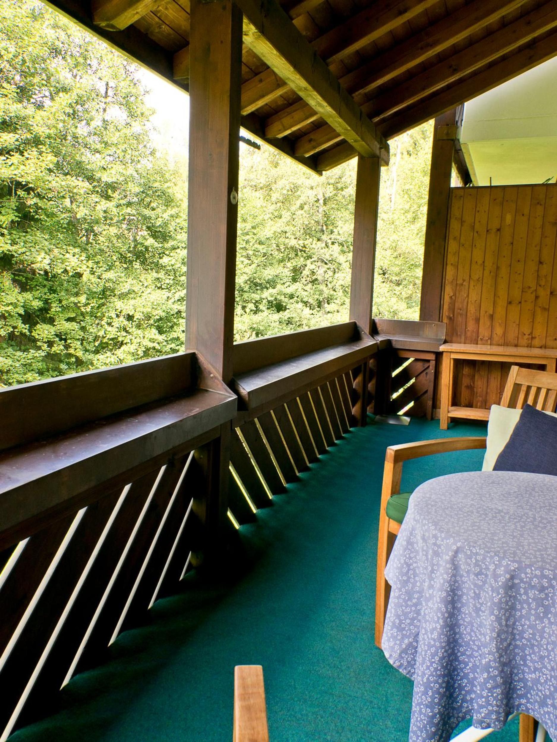 A room with a wooden bench, a bed with a floral bedspread, and a view of a forest through a window.