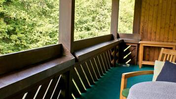 A room with a wooden bench, a bed with a floral bedspread, and a view of a forest through a window.
