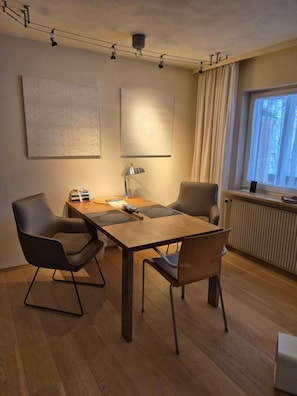 Ein modernes Zimmer mit einem Holztisch, zwei Stühlen, einer Lampe und einem Fenster mit Vorhängen.