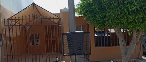 A gated entrance with a metal gate, a mailbox, and a tree in front of a building with a beige facade.