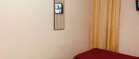 Una habitación con cama, televisor en la pared y cortina.