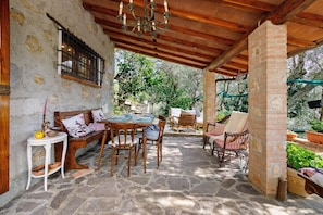 An outdoor patio with stone flooring, wooden furniture, and a brick wall. - Holiday Home 'Vacanza Tra Gli Olivi - Camaiore' with Wi-Fi and Air Conditioning (Camaiore)
