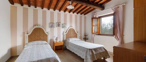 A room with two beds, a wooden ceiling, a window with curtains, and a small table.