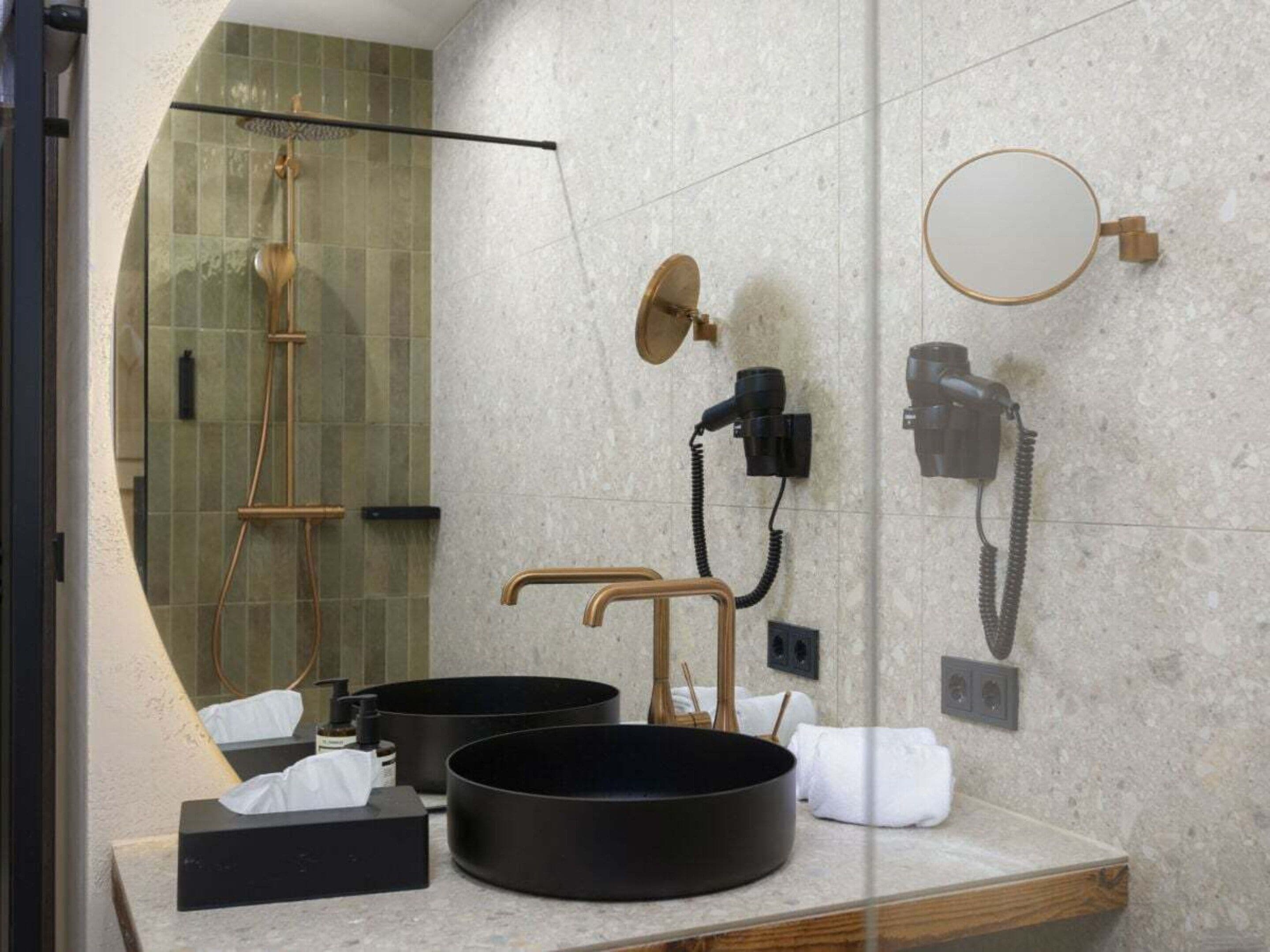 Un baño moderno con ducha envuelta en vidrio, un espejo redondo y un lavabo negro sobre el mostrador.