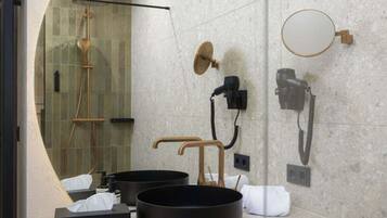Un baño moderno con ducha envuelta en vidrio, un espejo redondo y un lavabo negro sobre el mostrador.