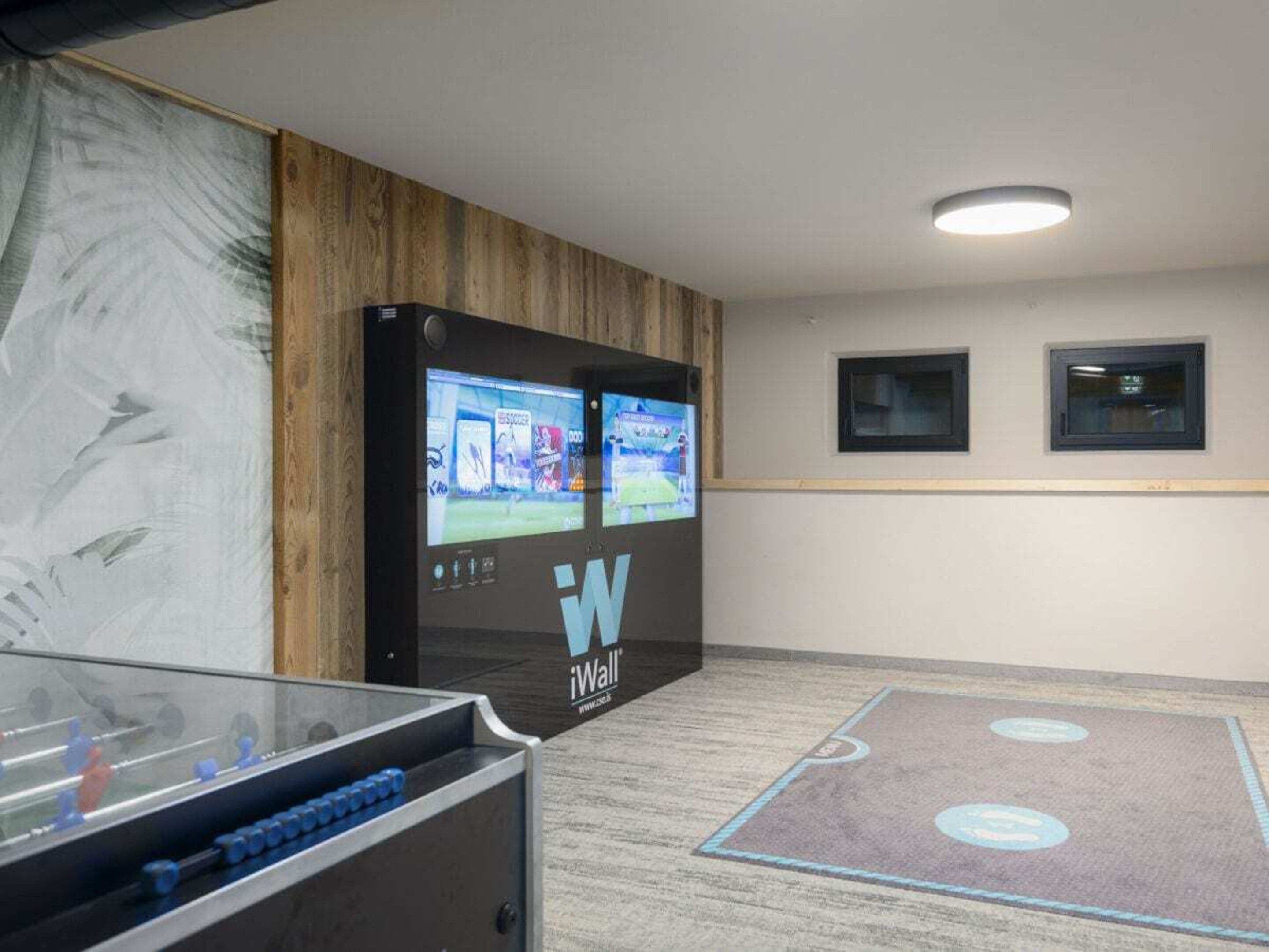 Quarto com um grande display interativo, duas janelas e um tapete com design circular.