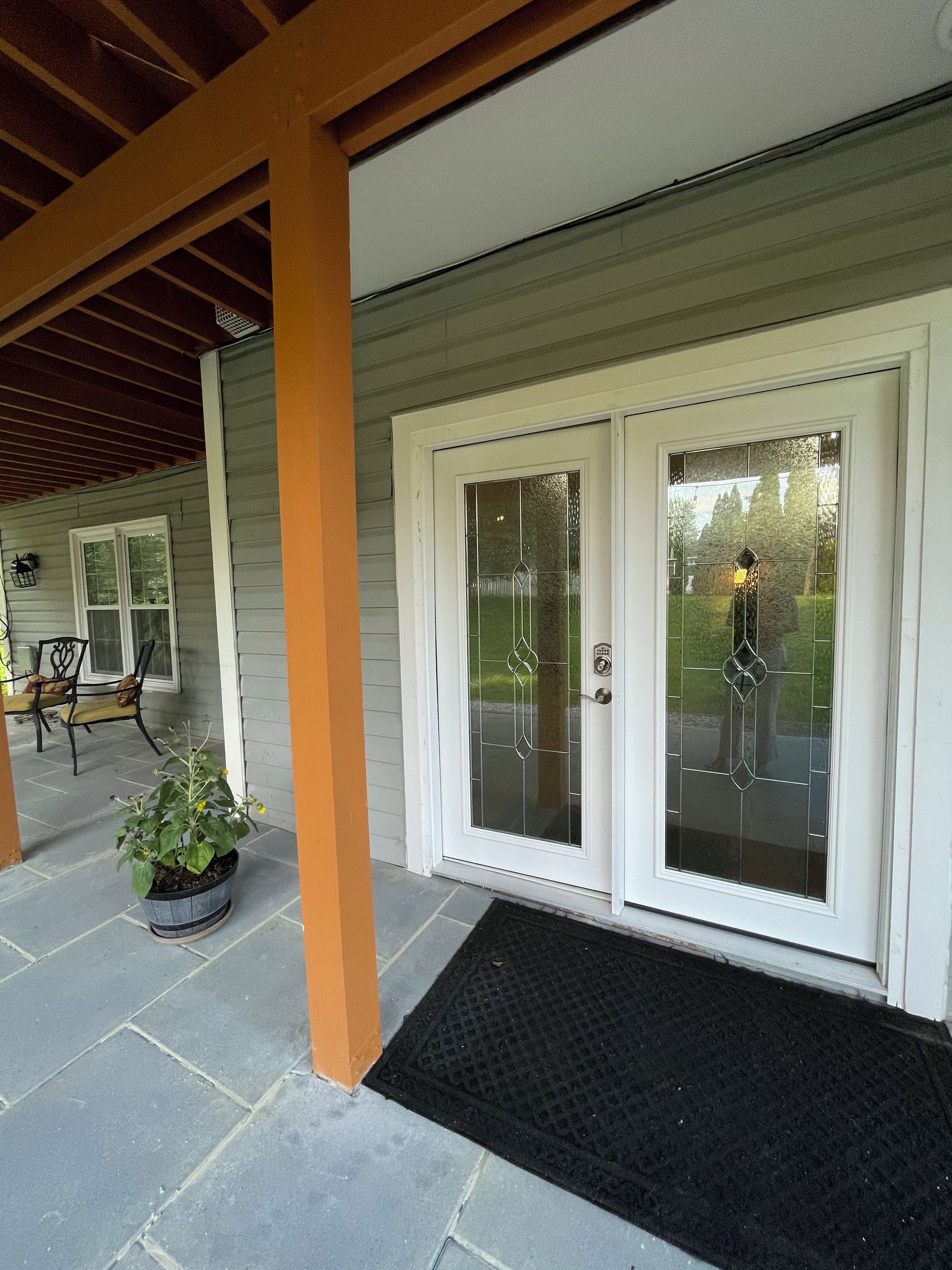 A covered porch with a potted plant, a bench, and a door with glass panels.