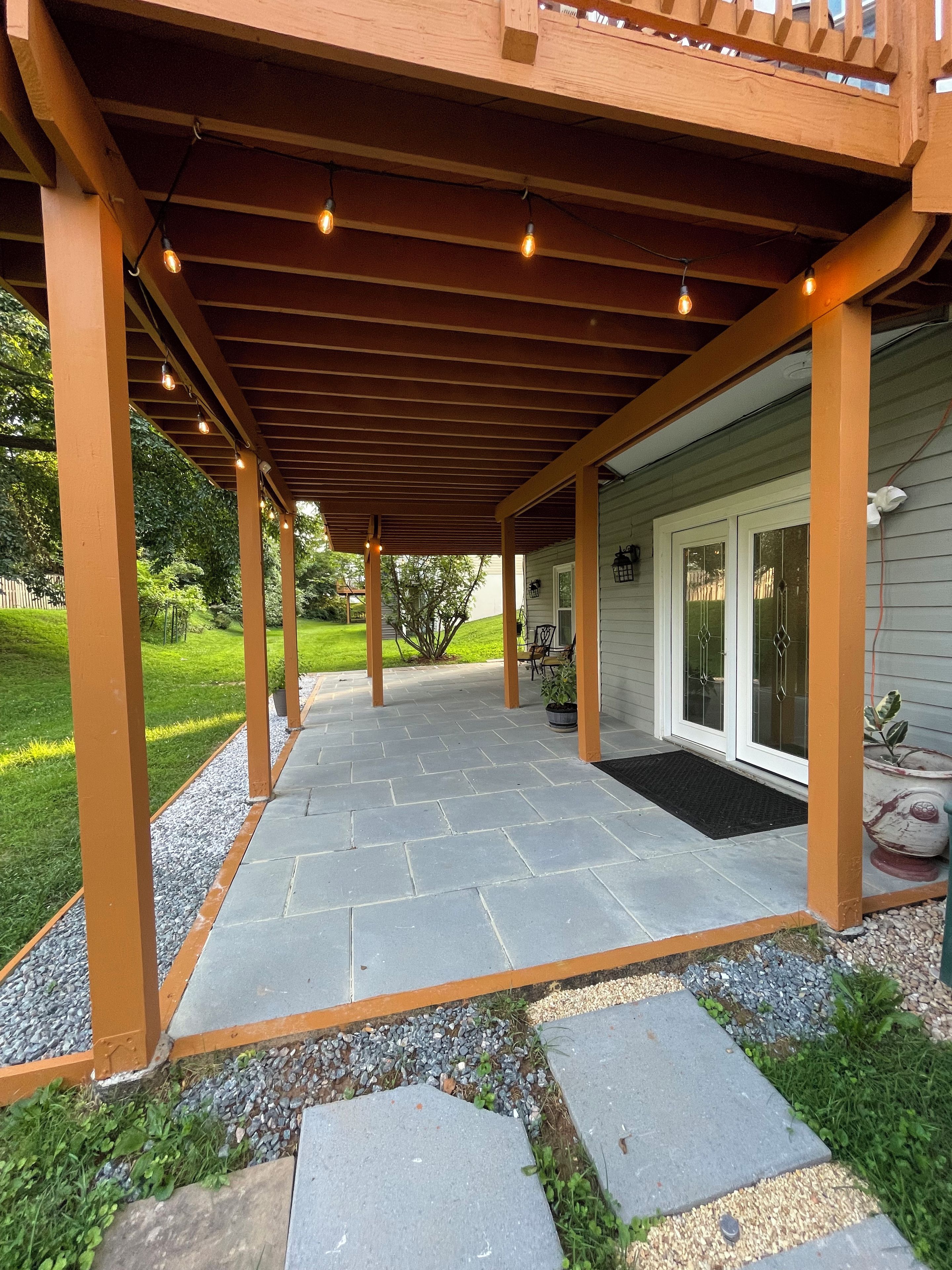 A covered patio area with stone flooring, wooden beams, and hanging lights.