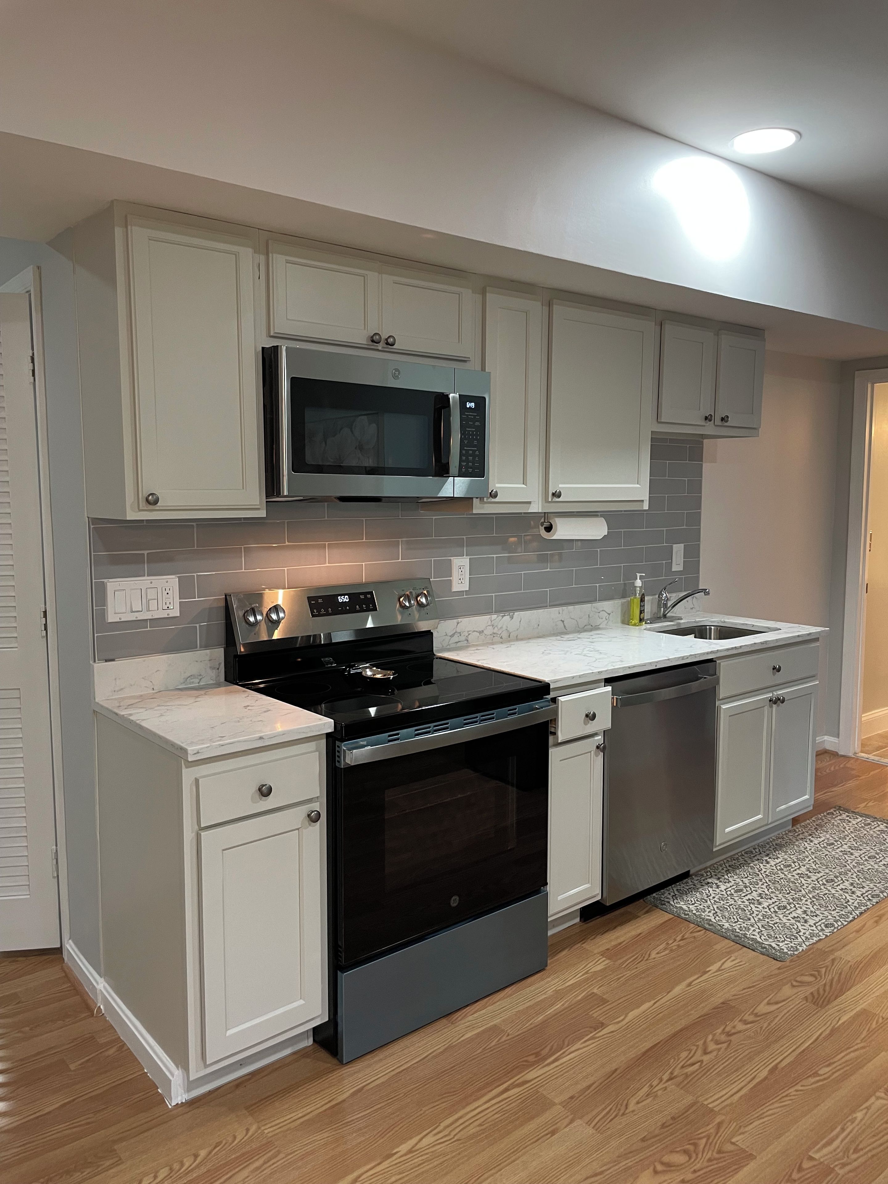 A kitchen with a built-in microwave, stove, and dishwasher, featuring light-colored cabinets and a marble countertop.