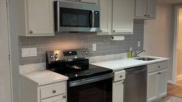 A kitchen with a built-in microwave, stove, and dishwasher, featuring light-colored cabinets and a marble countertop.