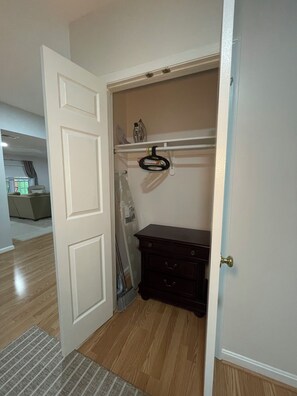 Een kamer met een houten vloer, een witte deur, een donker houten dressoir en een witte muur met een plank erboven.