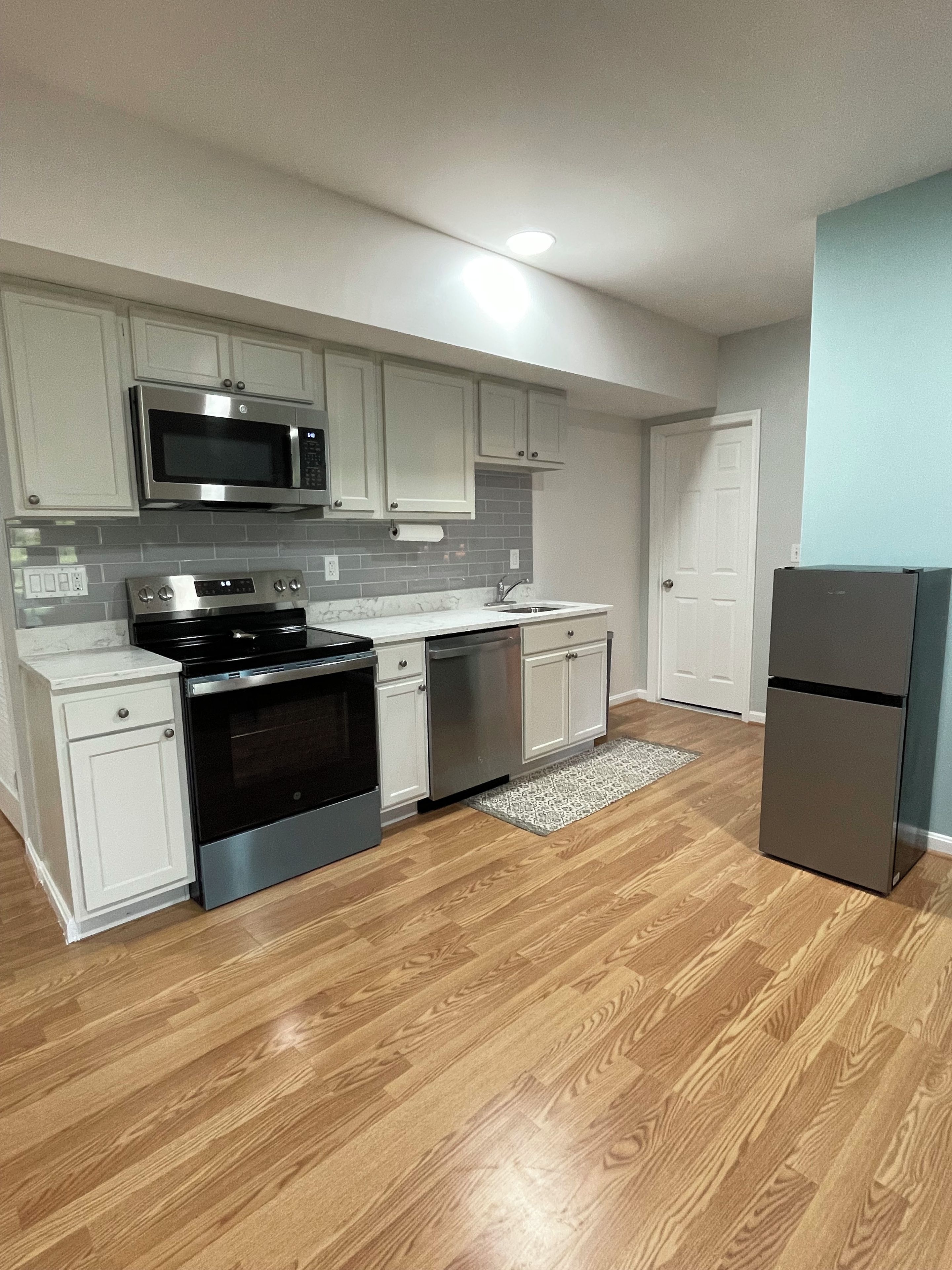 A modern kitchen with stainless steel appliances, white cabinetry, and a wooden floor.