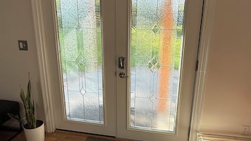 Una habitación con piso de madera, una puerta blanca con paneles de vidrio, una planta en maceta y un radiador.