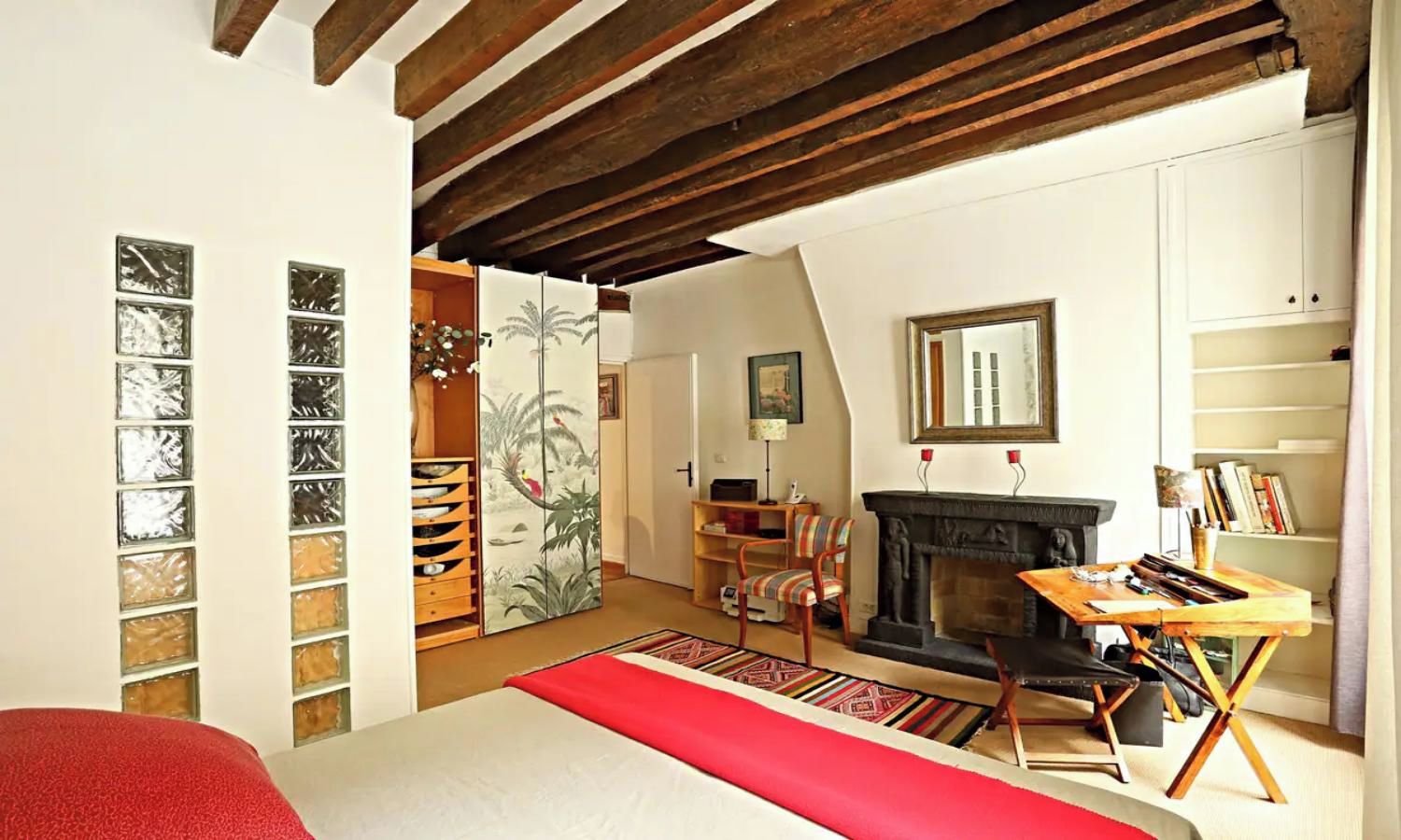 A bedroom with a bed, a fireplace, a desk, and a bookshelf.