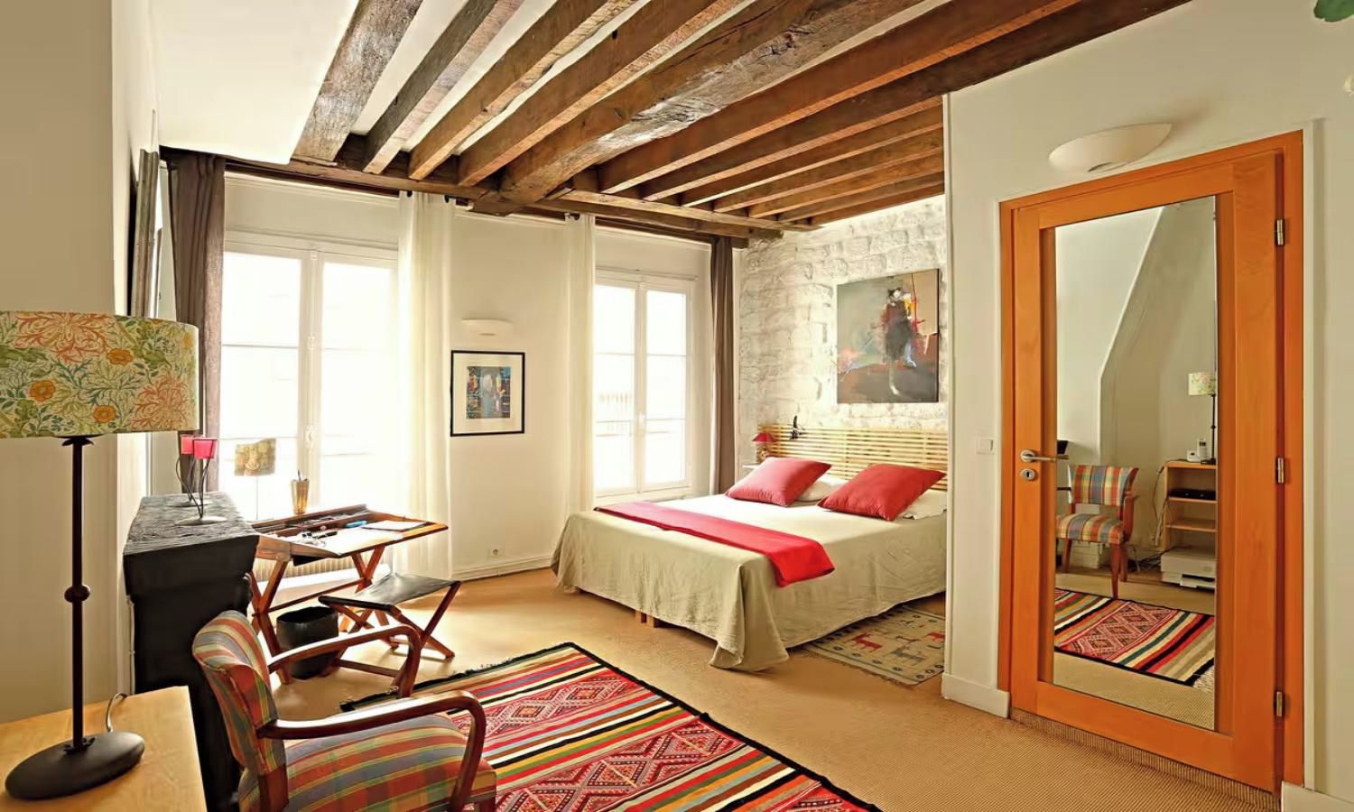 Un dormitorio con cama, escritorio, silla, espejo y puerta.