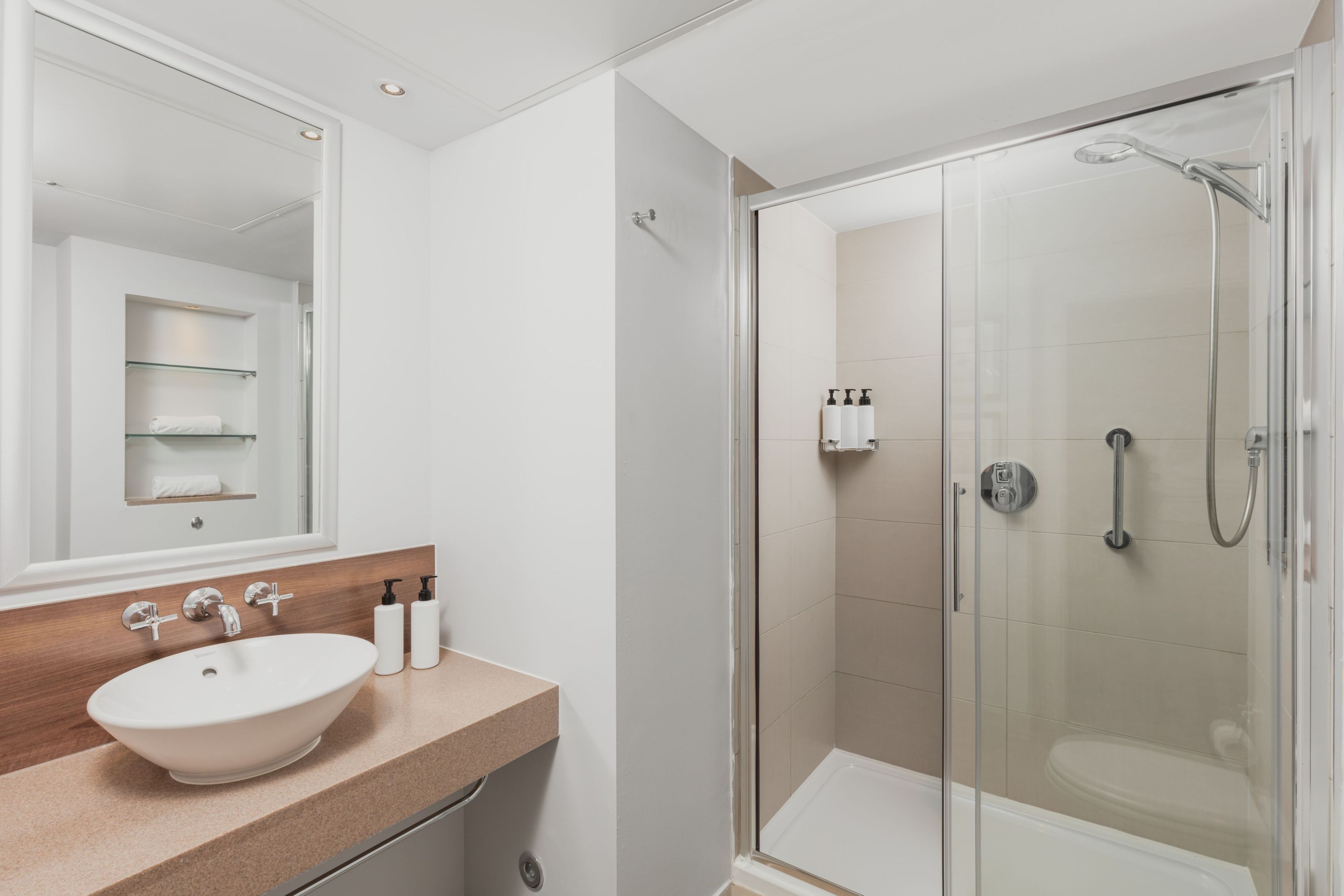A modern bathroom with a glass-enclosed shower, a white sink, and a mirror above it.