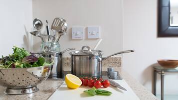 A kitchen with a colander, pots, a cutting board with tomatoes and a lemon, and a bowl of salad.
