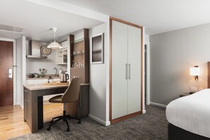 A hotel room with a kitchenette, a bed, a desk with a chair, a wardrobe, and a bedside table with a lamp. - Twin Studio Suite w/ Kitchenette | Free Breakfast (Newcastle Upon Tyne)
