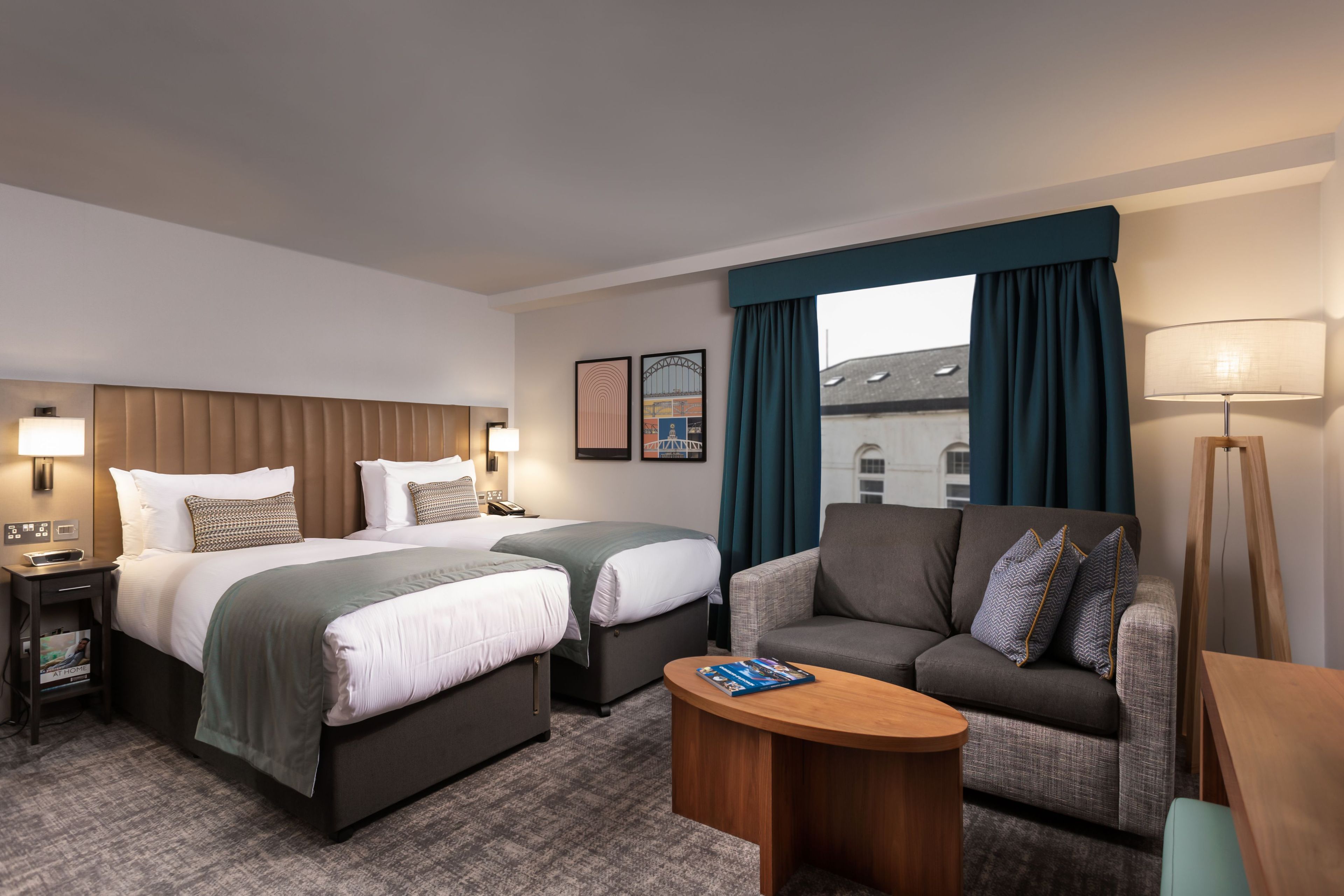 A hotel room with two beds, a sofa, a coffee table, and a lamp.