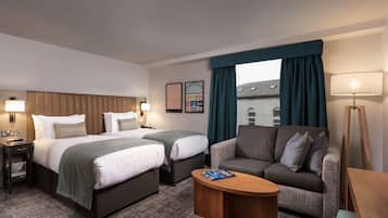 A hotel room with two beds, a sofa, a coffee table, and a lamp.