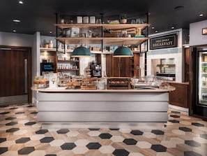 A breakfast bar with a coffee machine, shelves with jars, and a sign offering free breakfast. - Twin Studio Suite w/ Kitchenette | Free Breakfast (Newcastle Upon Tyne)