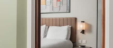 A hotel room with a bed, bedside table, lamp, and a wall-mounted artwork.