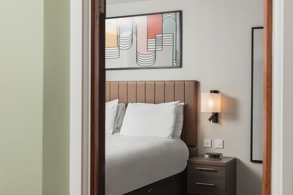 A hotel room with a bed, bedside table, lamp, and a wall-mounted artwork.