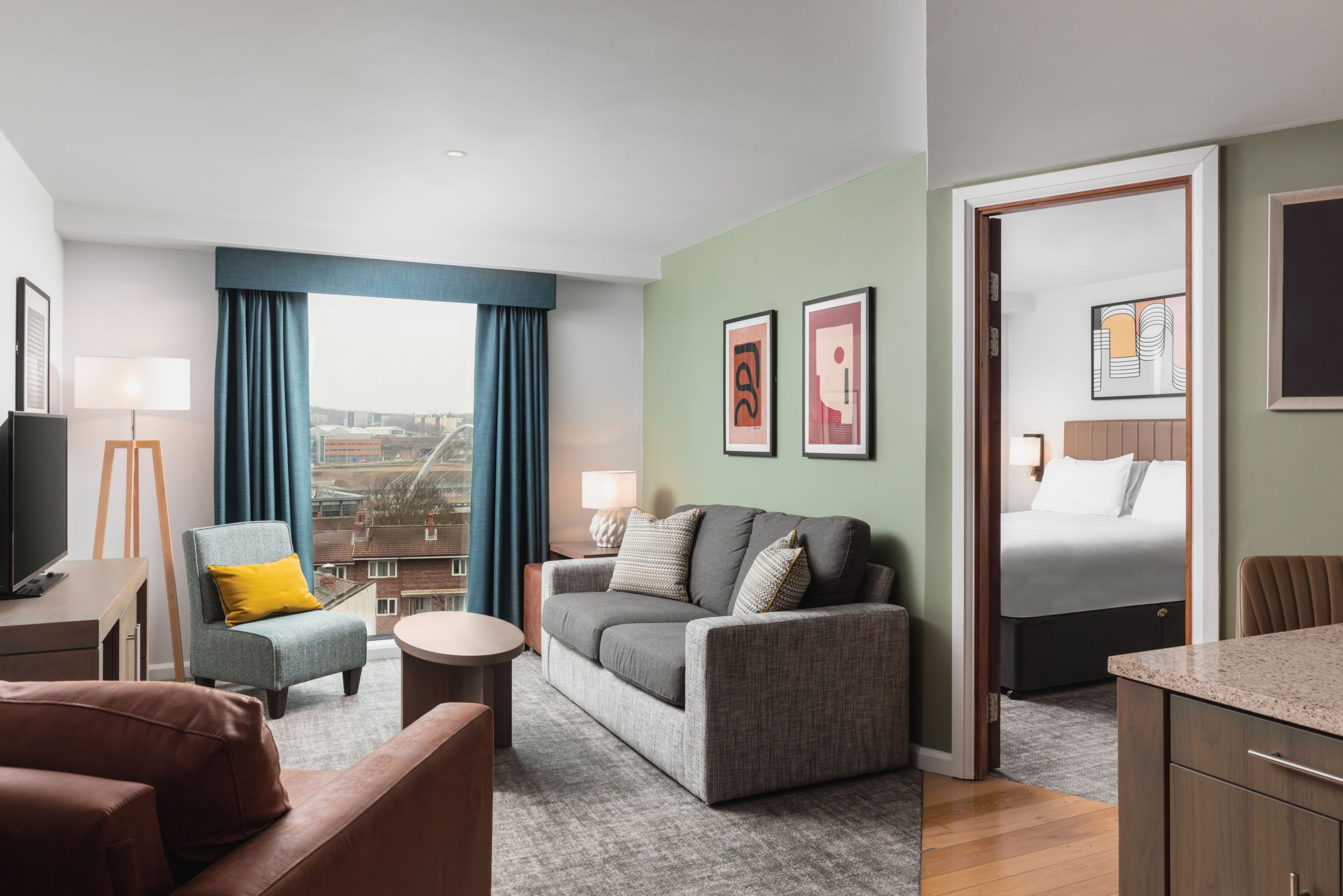 Habitación de hotel moderna con sofá, sillón y cama. Se ve una vista de la ciudad a través de la ventana, y la habitación tiene un diseño minimalista.