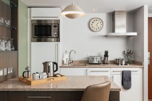 A modern kitchen with a microwave, toaster, kettle, and a clock on the wall. - Suite w/ Living Area + Kitchen | Free Breakfast! (Newcastle Upon Tyne)