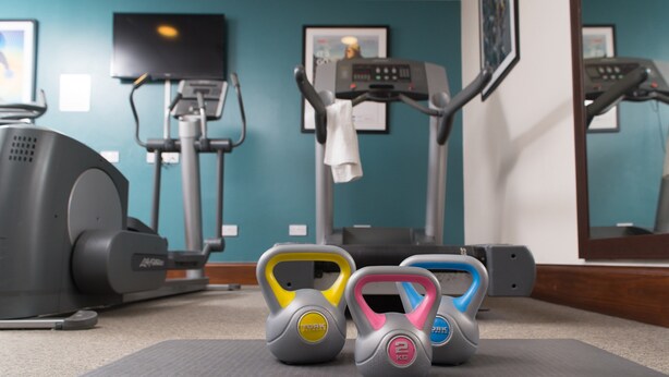 Ein Fitnessstudio mit Trainingsgeräten, darunter Laufband, Crosstrainer und Kettlebells.