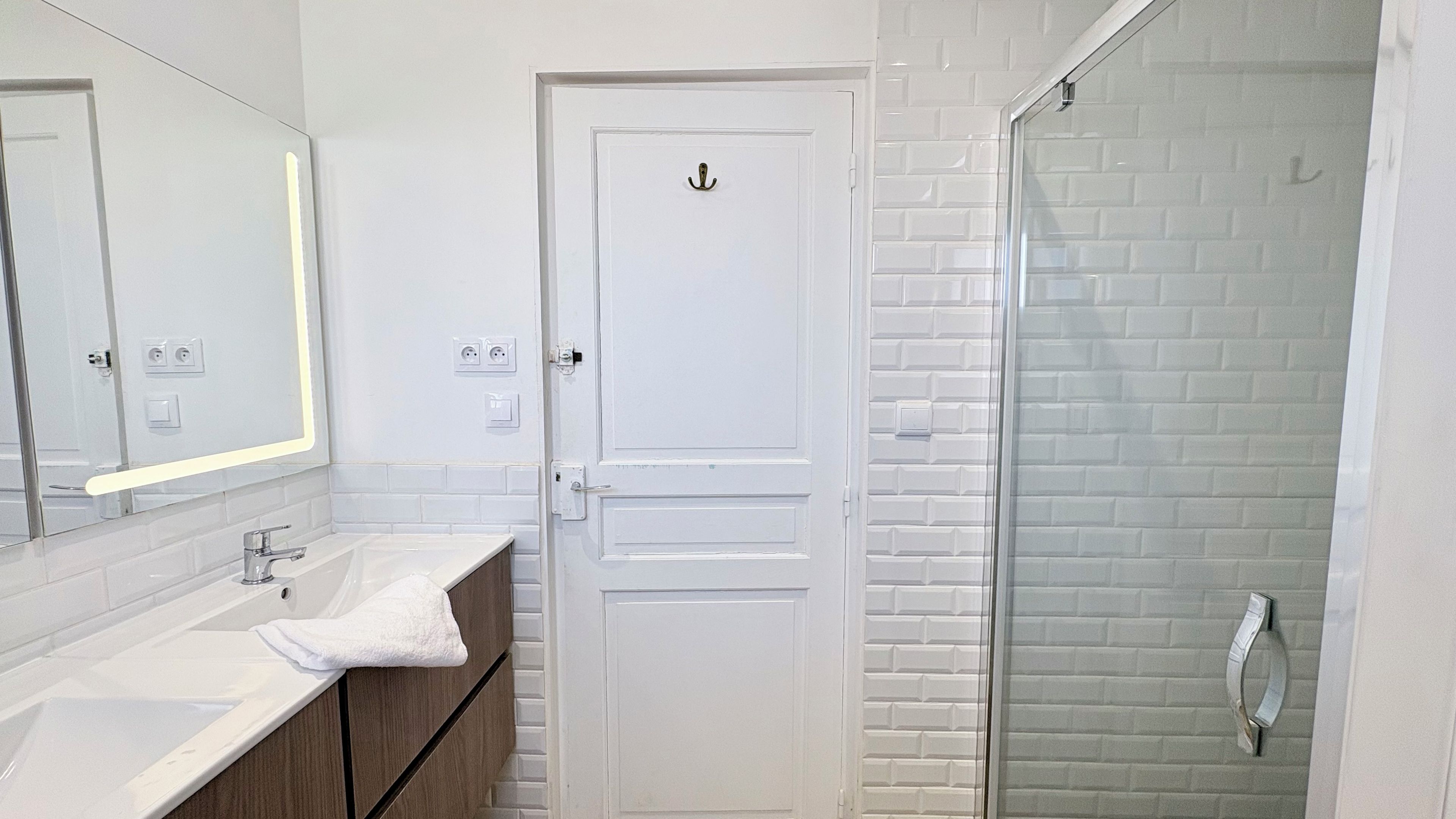 A bathroom with a white door, a glass shower enclosure, and a mirror above the sink.