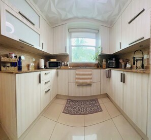 A modern kitchen with light wood cabinets, a microwave, and a window providing natural light. - Brisa Caribe Marbella Elegant 3BR Retreat Steps from Beach in Isla Verde, PR!! (Carolina)