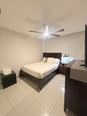 A bedroom with a bed, a ceiling fan, a bedside table with a lamp, and a dresser. - Brisa Caribe Marbella Elegant 3BR Retreat Steps from Beach in Isla Verde, PR!! (Carolina)