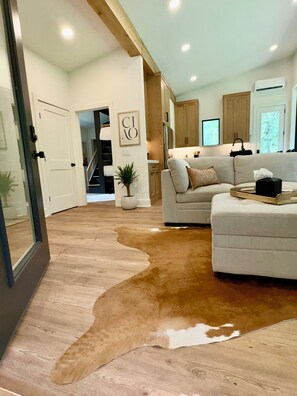 A modern living room with a cowhide rug, a sofa, and a dining area with wooden cabinets. - Brand New! - Luxury Modern Downtown Matthews-Hot Tub-EV-PuttingGreen- Walk2Shops (Matthews)