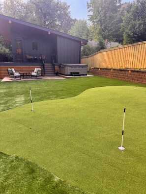 A backyard with a putting green, a hot tub, and a patio with chairs. - Brand New! - Luxury Modern Downtown Matthews-Hot Tub-EV-PuttingGreen- Walk2Shops (Matthews)