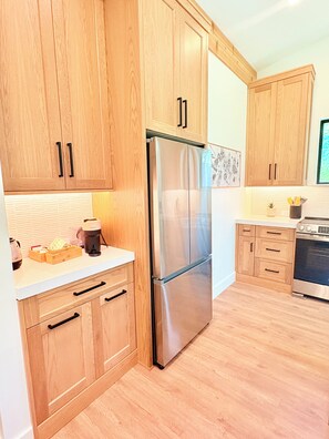 A kitchen with wooden cabinets, a stainless steel refrigerator, a coffee maker, and a stove. - Brand New! - Luxury Modern Downtown Matthews-Hot Tub-EV-PuttingGreen- Walk2Shops (Matthews)