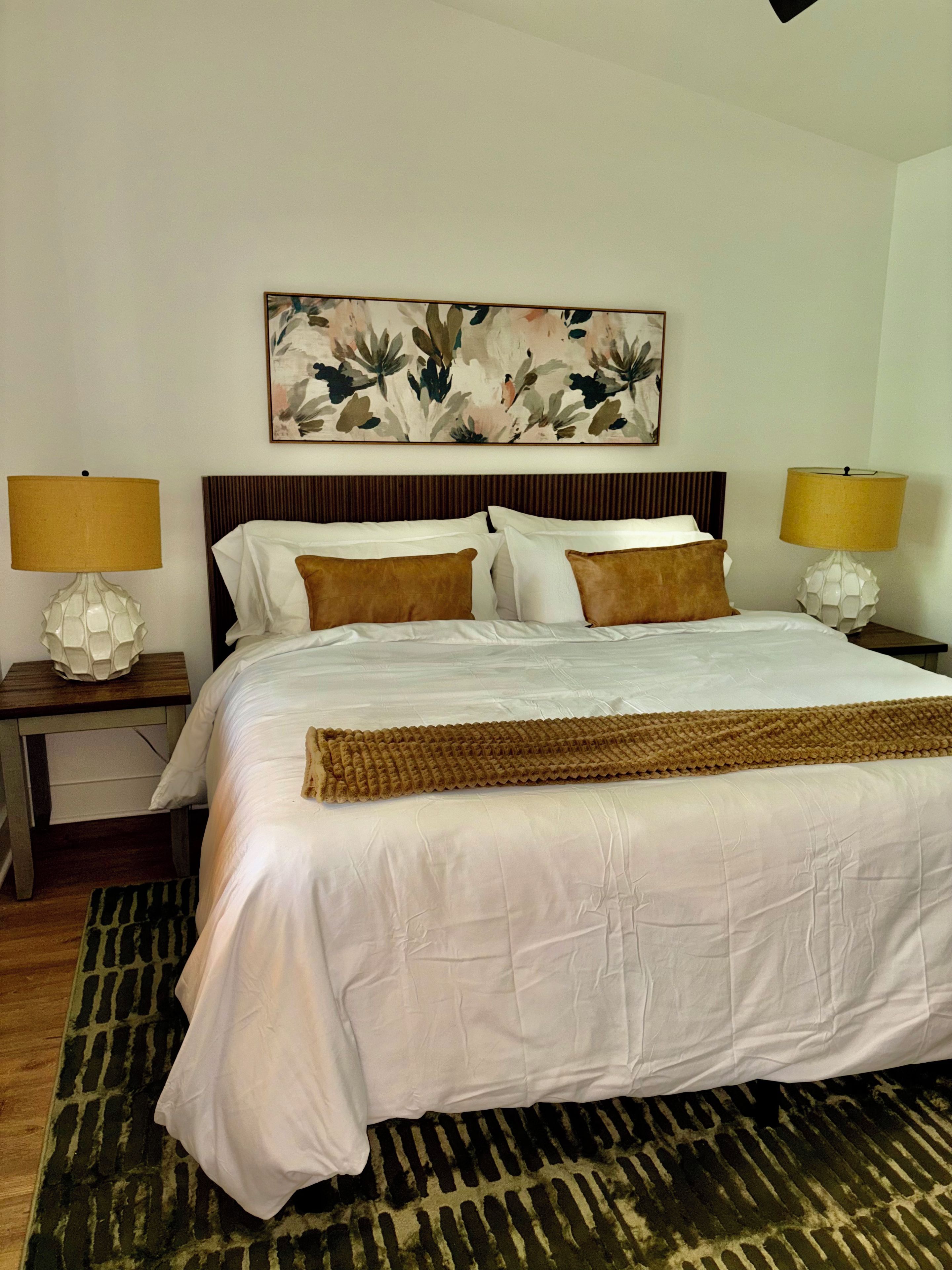 A hotel room with a large bed, two bedside tables, a decorative wall piece, and a patterned rug.