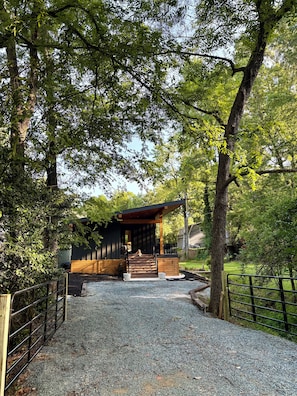 A gravel pathway leading to a wooden structure with a covered entrance, surrounded by trees. - Brand New! - Luxury Modern Downtown Matthews-Hot Tub-EV-PuttingGreen- Walk2Shops (Matthews)