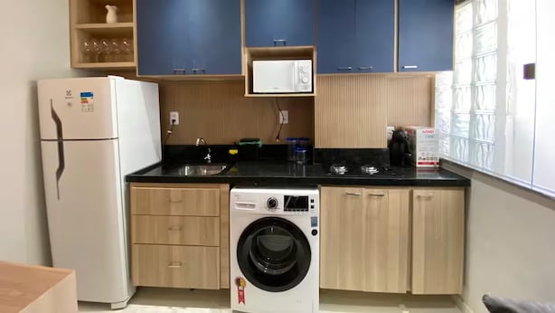 A compact kitchen with a refrigerator, washing machine, and a window with blinds. - 302 - 2 Bedrooms Charming (Belém)