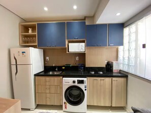 A compact kitchen with a refrigerator, washing machine, and a window with blinds. - 302 - 2 Bedrooms Charming (Belém)