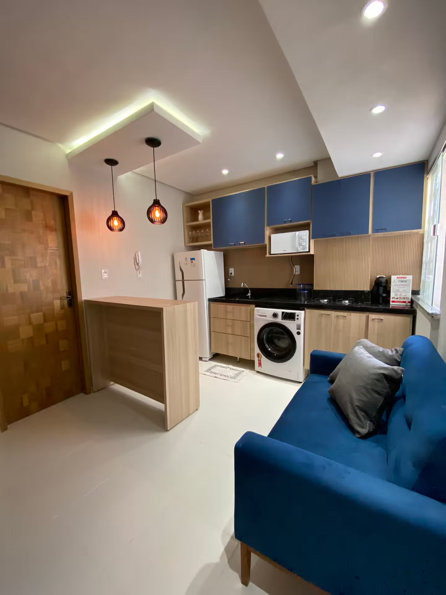A modern kitchen with a built-in washing machine, a blue sofa, and pendant lighting.