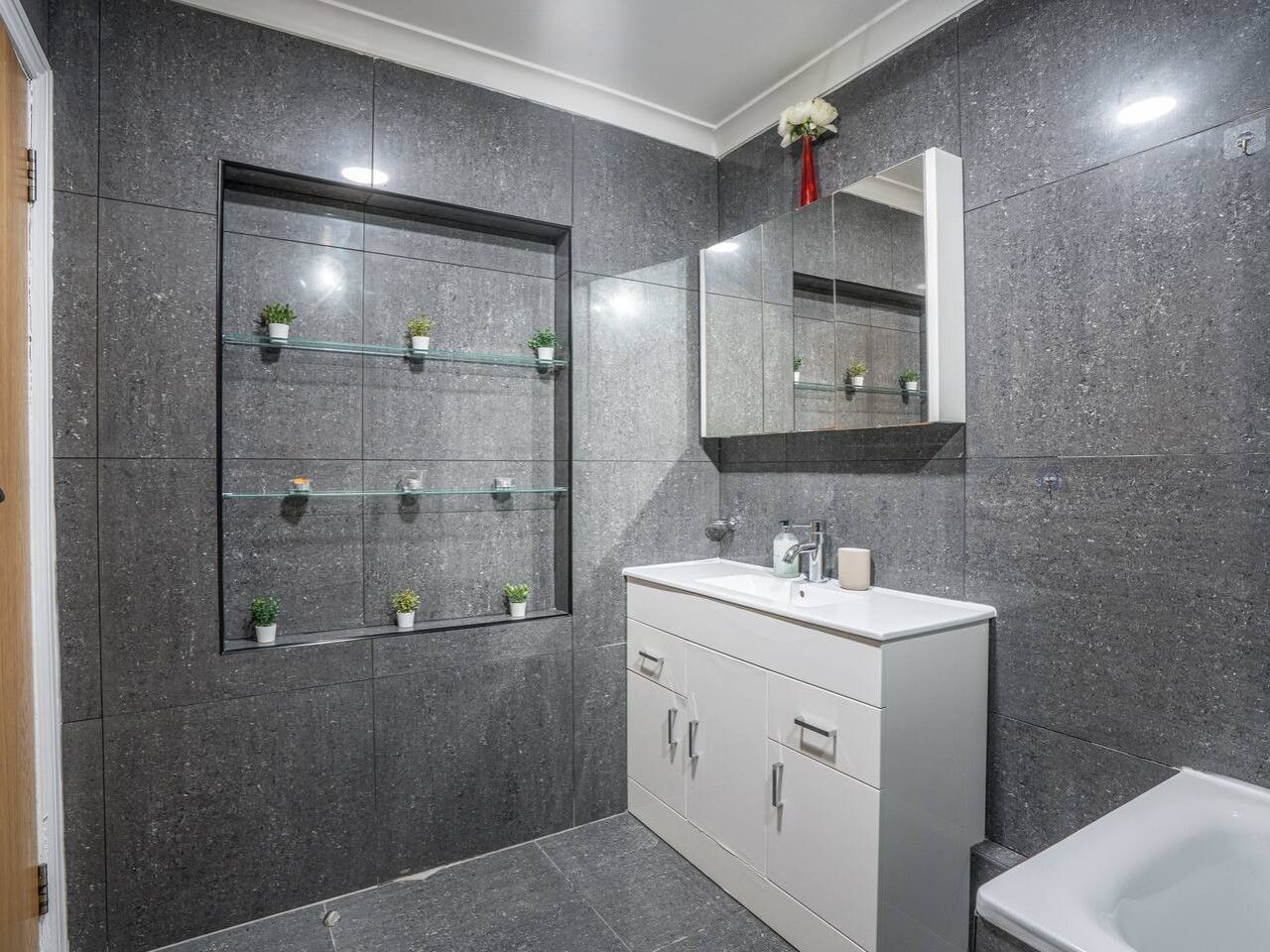 A modern bathroom with a large mirror, a white vanity, and a glass shelf with potted plants.