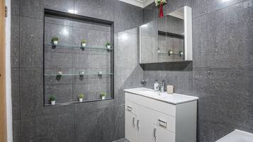 A modern bathroom with a large mirror, a white vanity, and a glass shelf with potted plants.