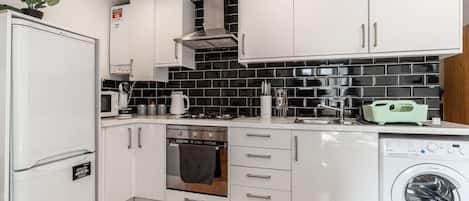 A compact kitchen with white cabinets, a built-in oven, a microwave, and a washing machine.