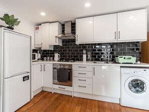 A compact kitchen with white cabinets, a built-in oven, a microwave, and a washing machine. - Cosy 1BR Flat | West Kensington | Sleeps 5 |London (Greater London)