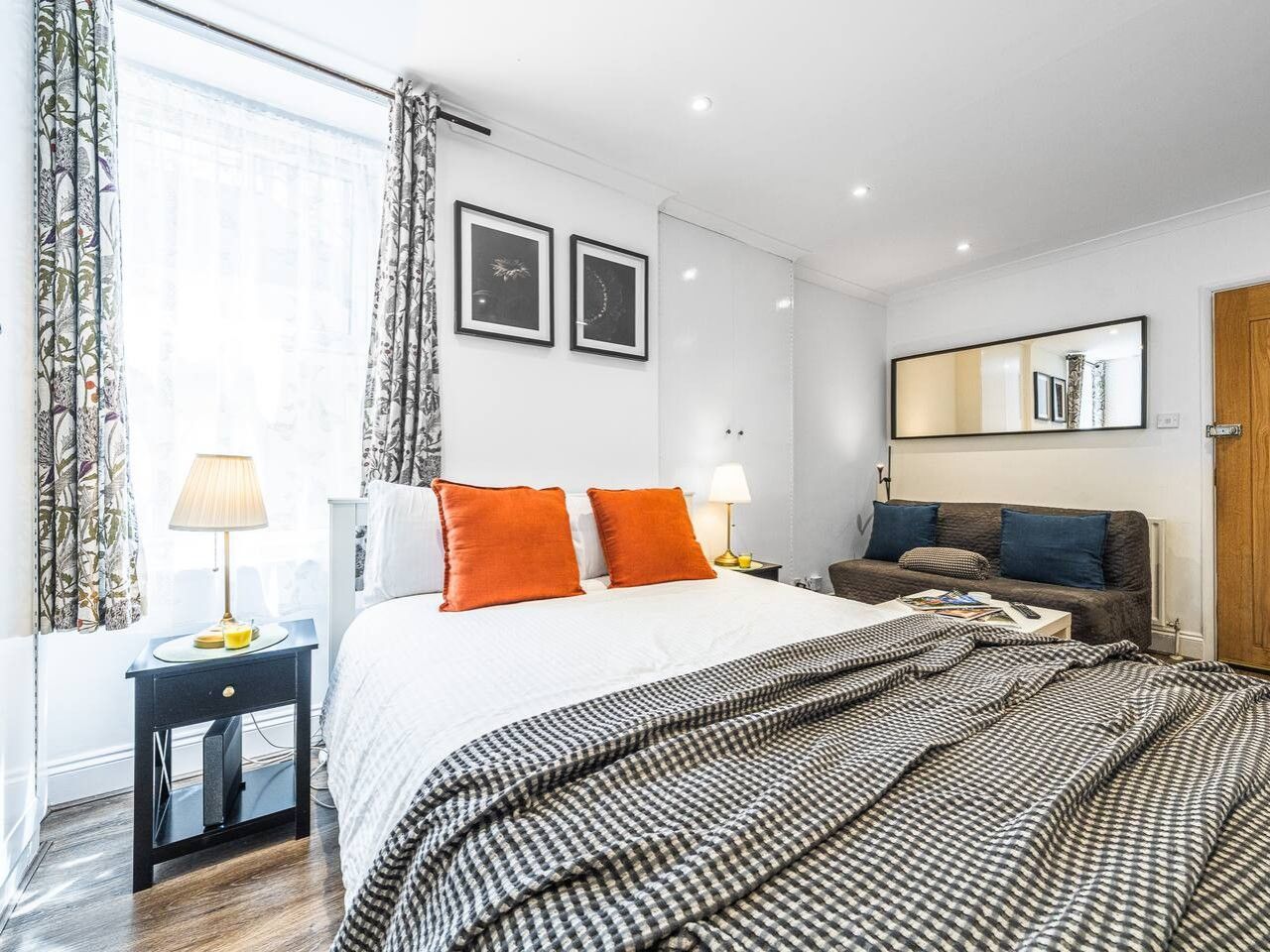 A hotel room with a bed, bedside tables, a sofa, and a large mirror.