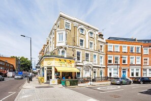 A street view with a cafe named 'Crazy Coffee' on the corner, adjacent to a row of terraced houses. - Elegant West Kensington Studio | Central London (Greater London)