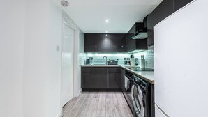 Una cocina moderna con armarios oscuros, lavavajillas y un refrigerador blanco.